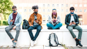 Image of 4 friends looking at their phones while sitting on a wall. Social connections can help when you are dealing with depression symptoms. Building support is what to do for depression. A depression therapist can also help with this.